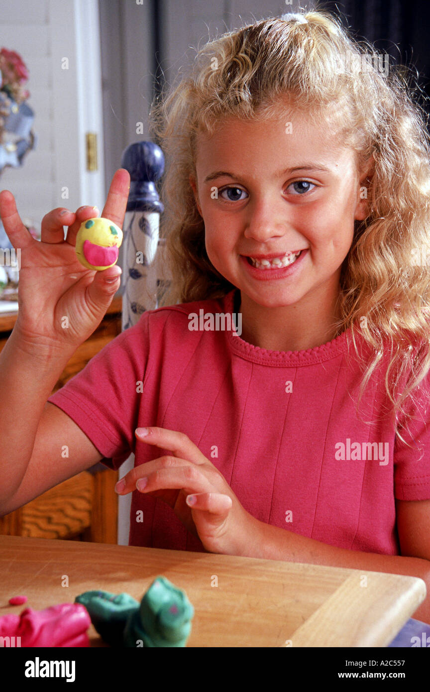 Kaukasische Mädchen 8-10 Jahre alte Stück Teig Ton-Gesicht, genießen Sie ruhige Zeit am Tisch ziemlich niedlich locken Grübchen gekräuselt Haar halten POV Stockfoto