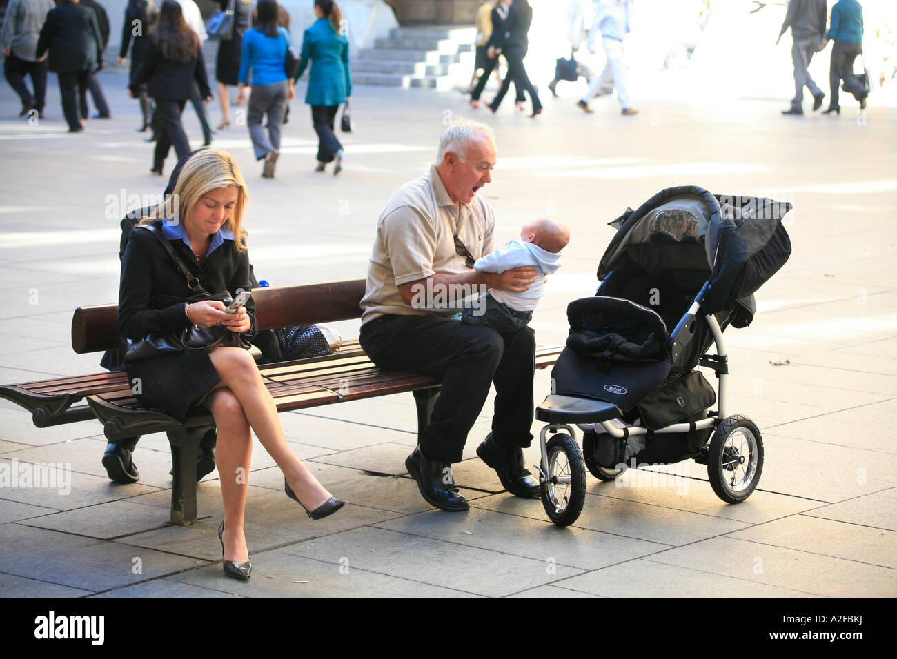 Großvater spielt mit Baby, während eine junge blonde Frau mit ihrem Handy spielt. Stockfoto