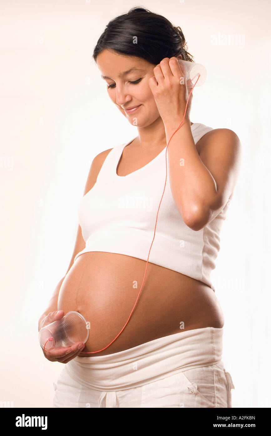 Schwangere Frau mit Cup am Bauch und Ohr Stockfoto