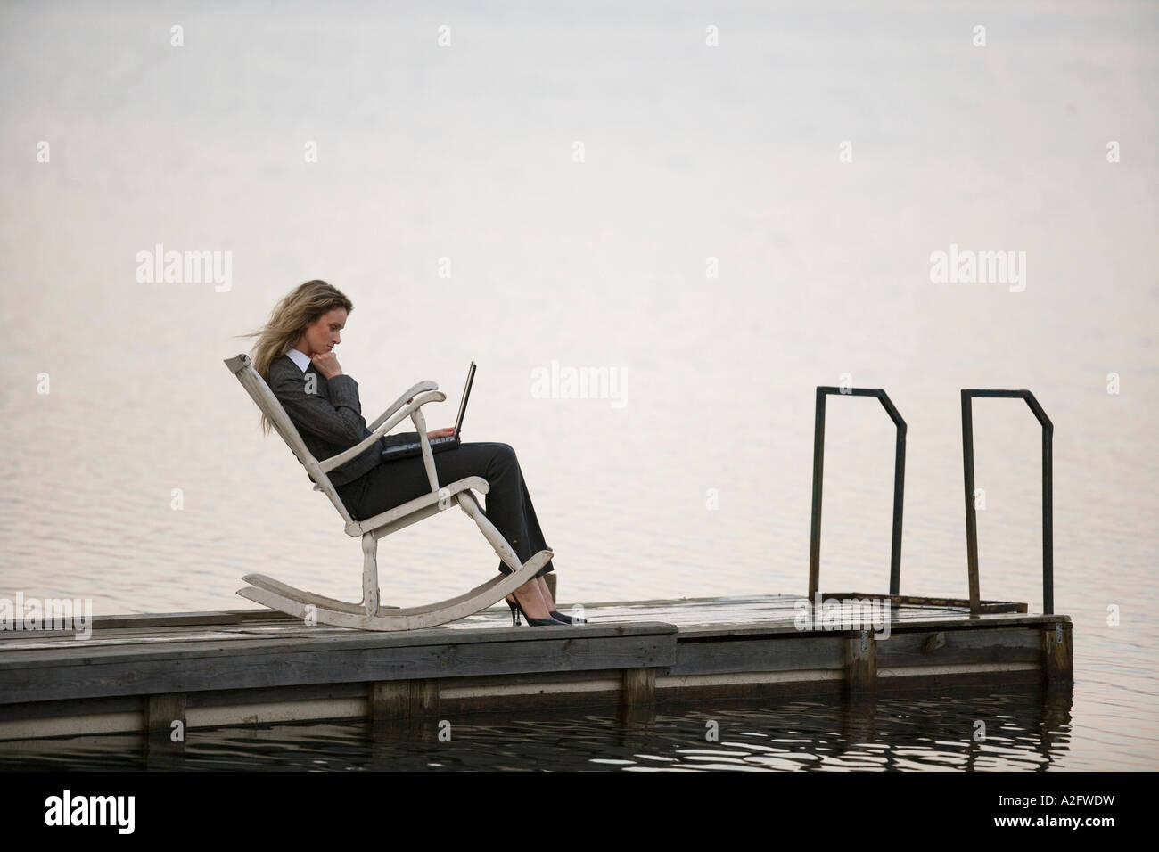 Geschäftsfrau im Schaukelstuhl auf Steg sitzen, mit Laptop, Seitenansicht Stockfoto