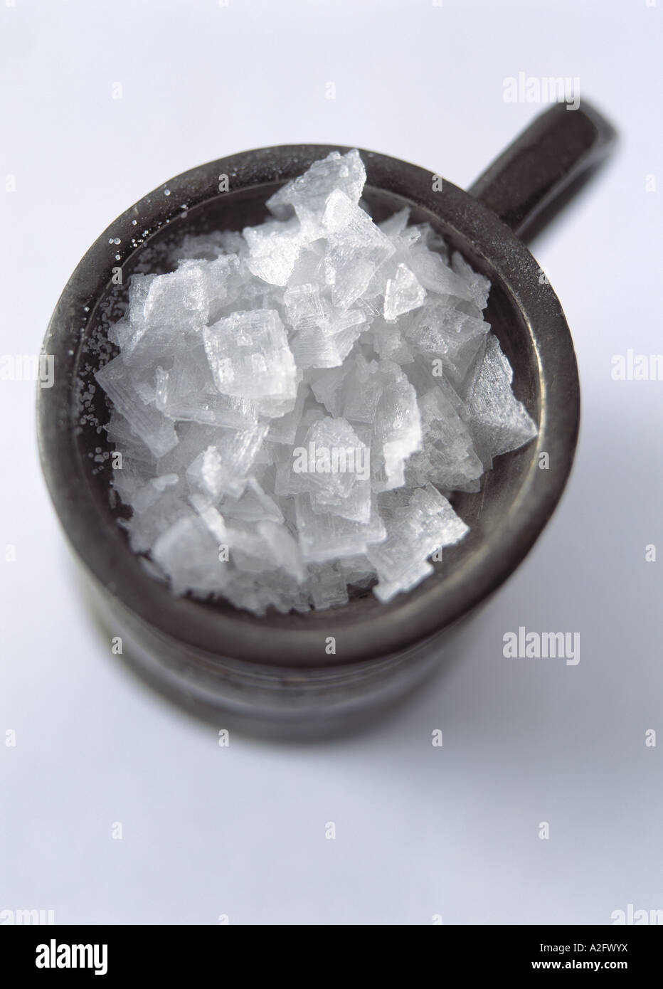 Ein Zinn Krug voll von Steinsalz-Kristalle auf weißem Hintergrund Stockfoto