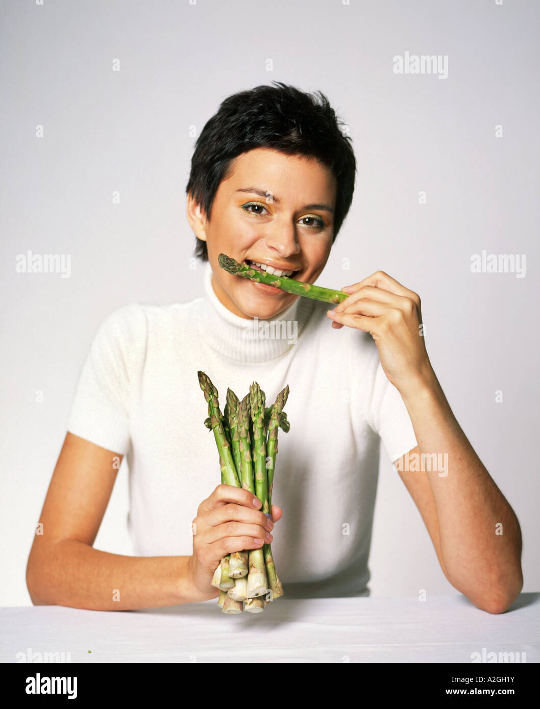 1208154 indoor Studio junge Frau Brünette kurze Haare 25 20 weißen Pullover Jersey halten Gemüse Spargel Bündel Sit Tabelle sterben Stockfoto