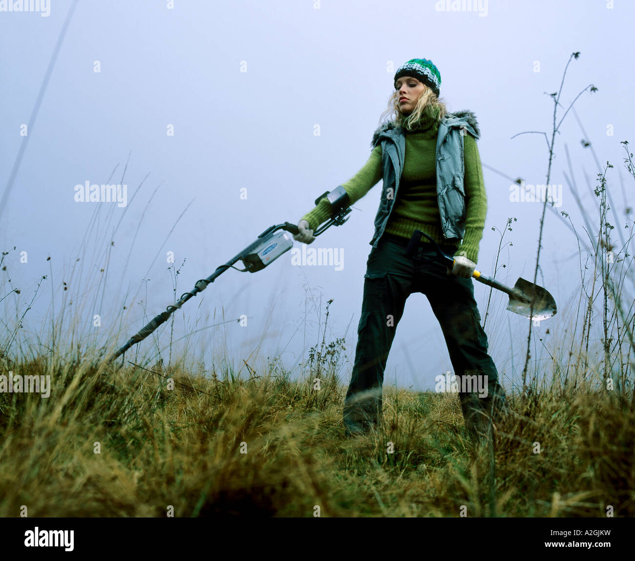 1212971 Outdoor-Tag im Herbst Frau junge 25 30 blonde langhaarige Wiese Feld Rasen Stand aussehen Weste blau Handschuh Handschuhe Stockfoto