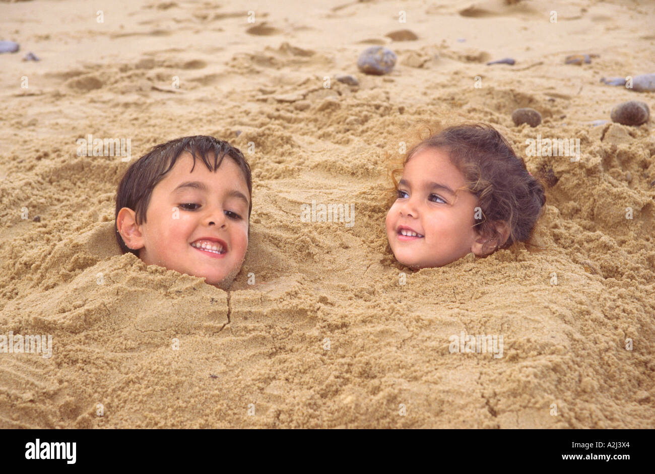 Zwei junge Kinder begraben im Sand am StrandNorfolk Stockfotografie