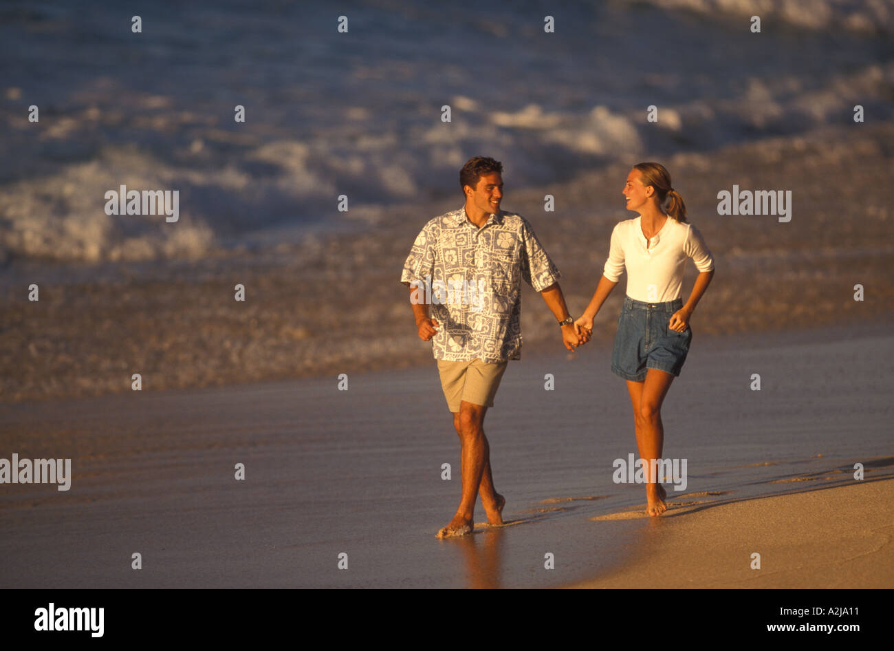 Leger gekleidet, barfuß paar sehen einander an, wie sie Hand in Hand im nassen Sand des Strandes Fuß Stockfoto