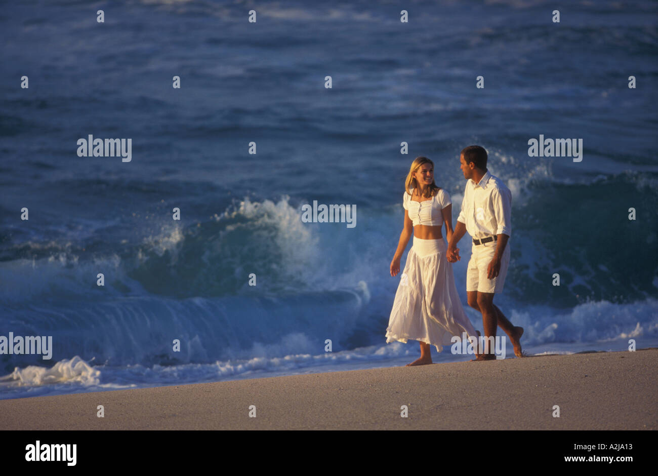 Leger gekleidet, barfuß paar sehen einander an, wie sie Hand in Hand am Strand als Wellen brechen sich im Hintergrund gehen Stockfoto