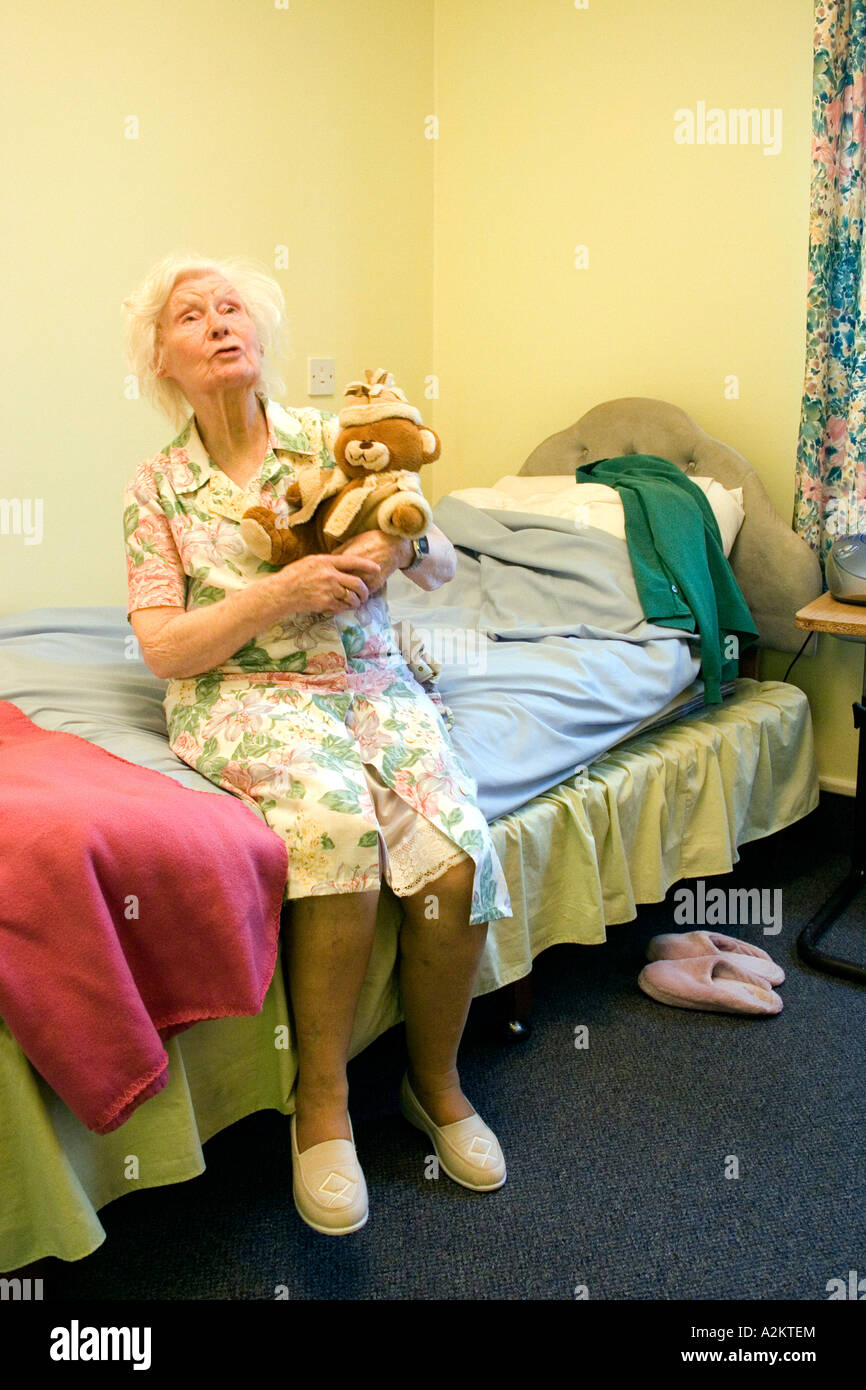 traurige alte Dame im Pflegeheim mit Altersdemenz sitzen auf der Bettkante mit Teddybär Stockfoto