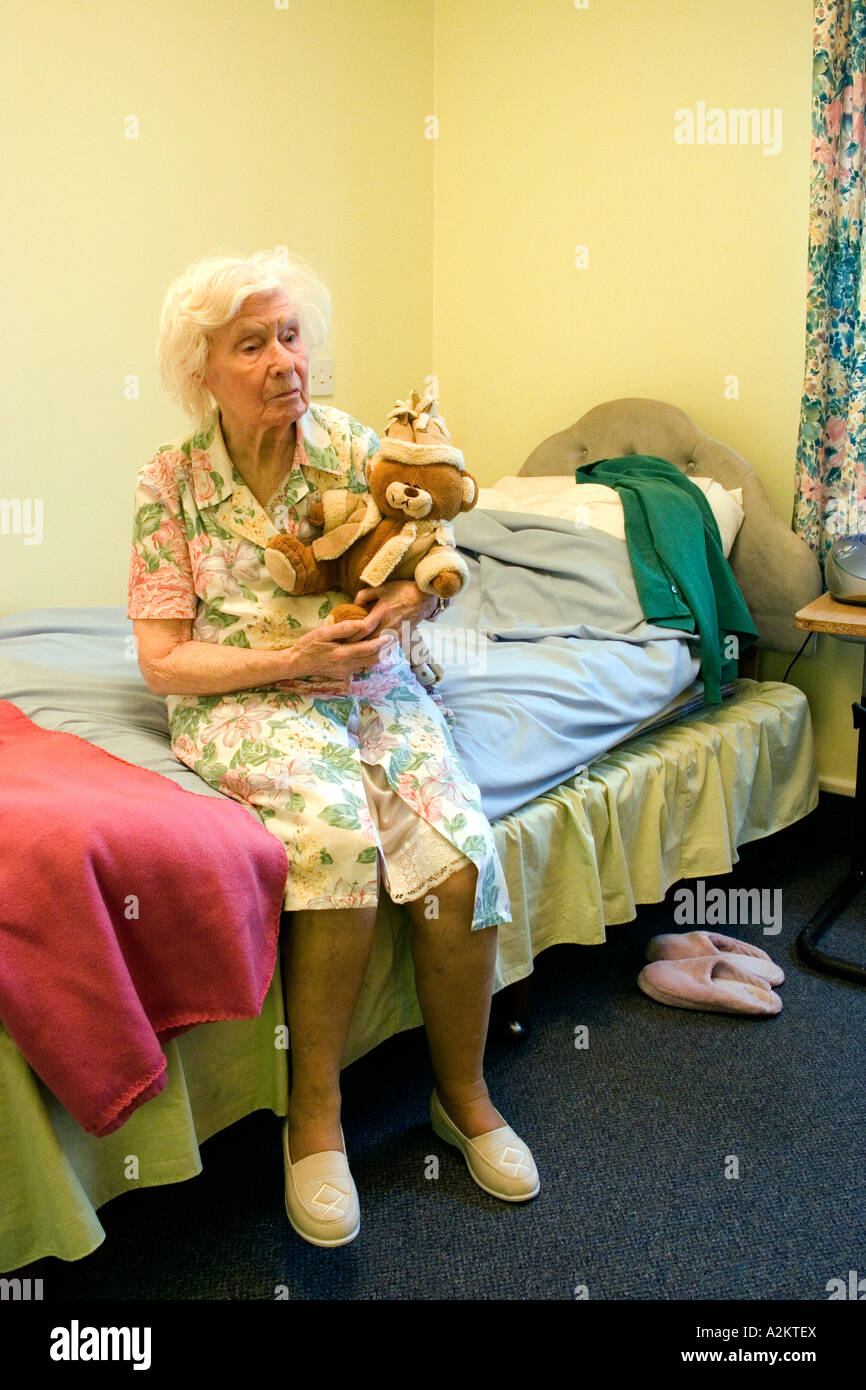 feierliche alte Dame im Pflegeheim mit Altersdemenz sitzen auf der Bettkante mit Teddybär Stockfoto