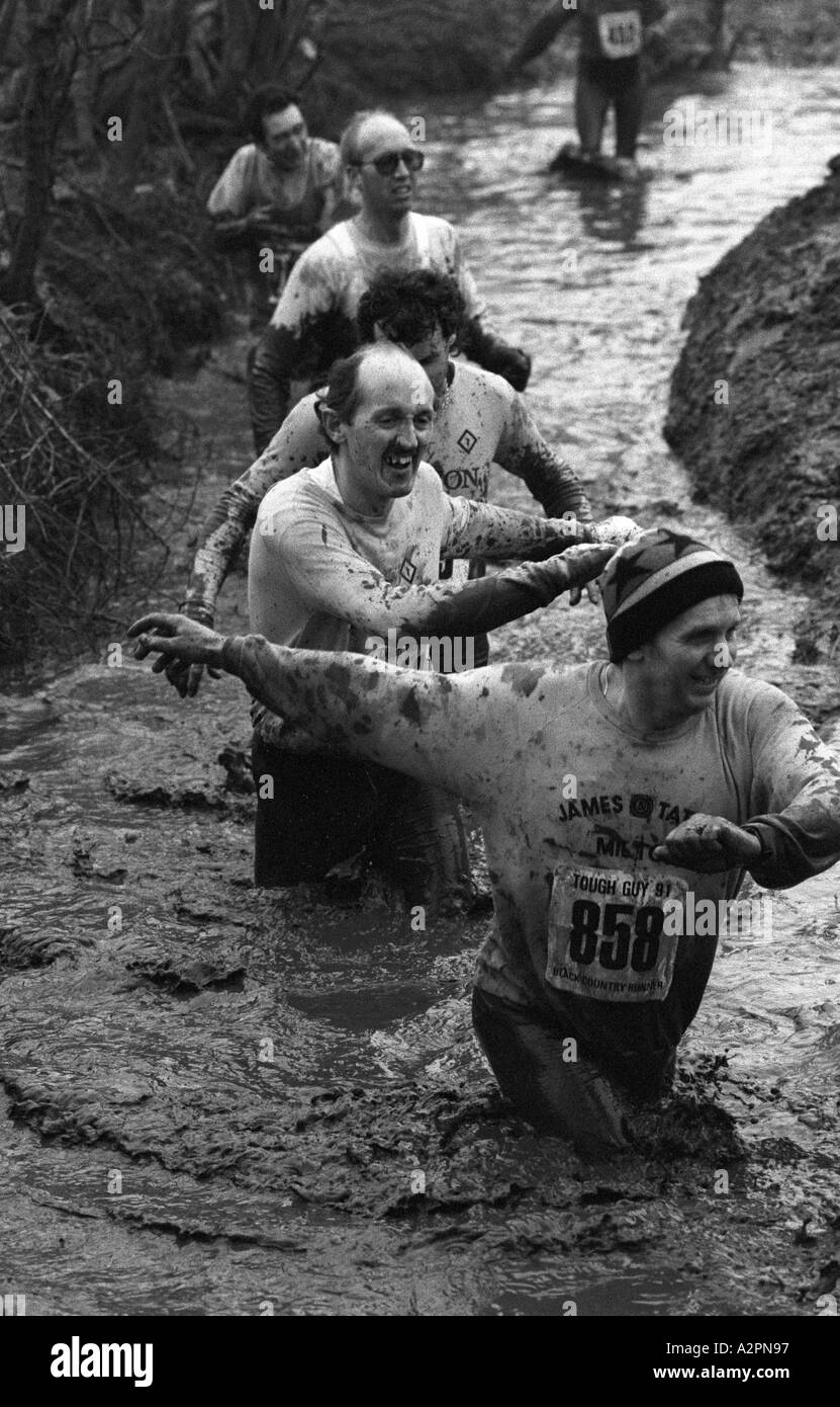 Wettbewerber waten in kaltem schlammigen Strom Tough Guy Rennen bei Tettenhall, West Midlands, England, UK 1991 Stockfoto