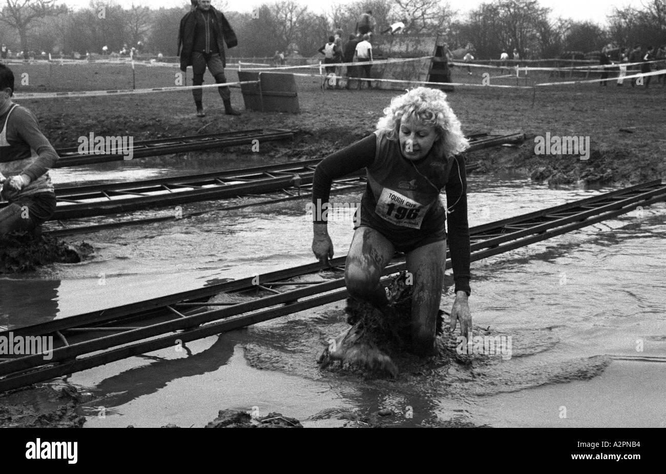 Frau Konkurrent waten durch kaltes Schmutzwasser Tough Guy Rennen bei Tettenhall, West Midlands, England, UK 1991 Stockfoto