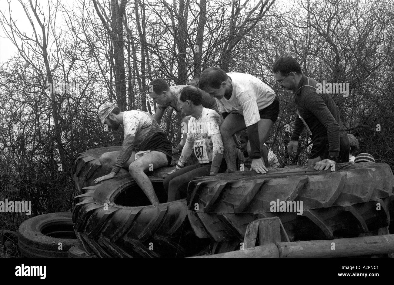 Konkurrenten, die alten Reifen Hindernis Tough Guy Rennen bei Tettenhall, West Midlands, England, UK 1991 Überklettern Stockfoto
