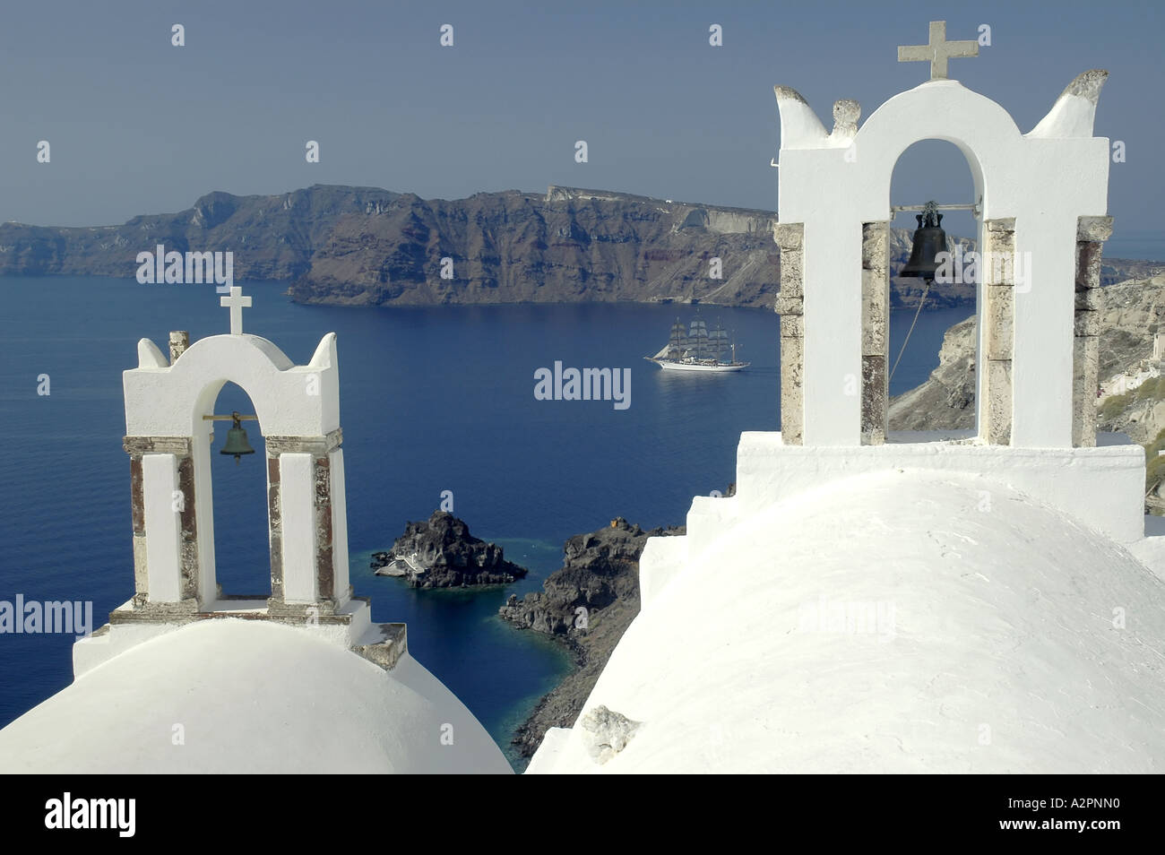 Zwei Glockenturm mit Blick auf die Caldera in Oia, Santorini, griechische Inseln mit Boot im Hintergrund Stockfoto