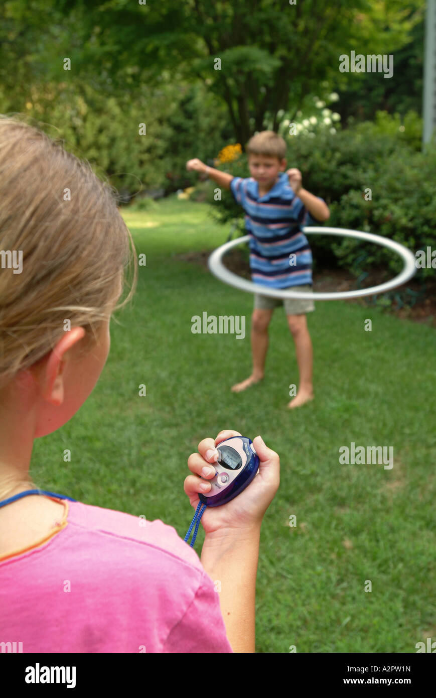 10 Jahre altes Mädchen verwendet eine digitale Stoppuhr zur Zeit 7 Jahre alten Bruder tun mit einem Hula Hoop Reifen Stockfoto