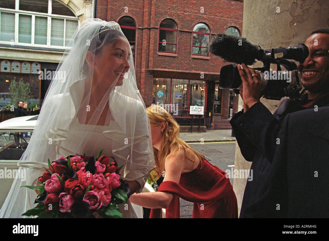 Braut ankommt in der Kirche von ihren Brautjungfern und Pageboys und Videofilmer begrüßt Stockfoto
