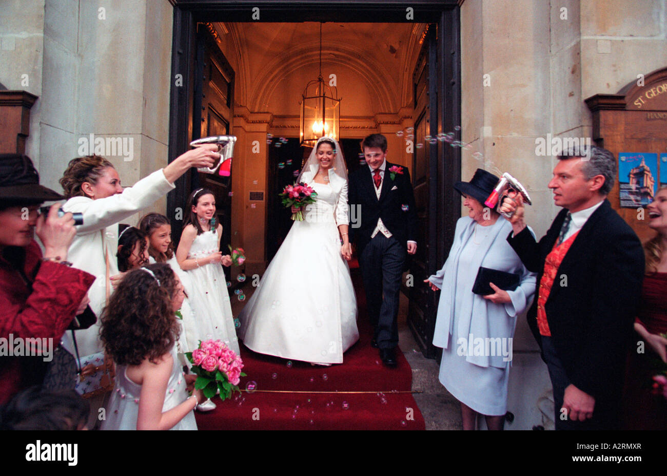 Frisch verheiratete Braut und Bräutigam, die St.-Georgs-Kirche London winkte auf Familie und Freunde zu verlassen Stockfoto