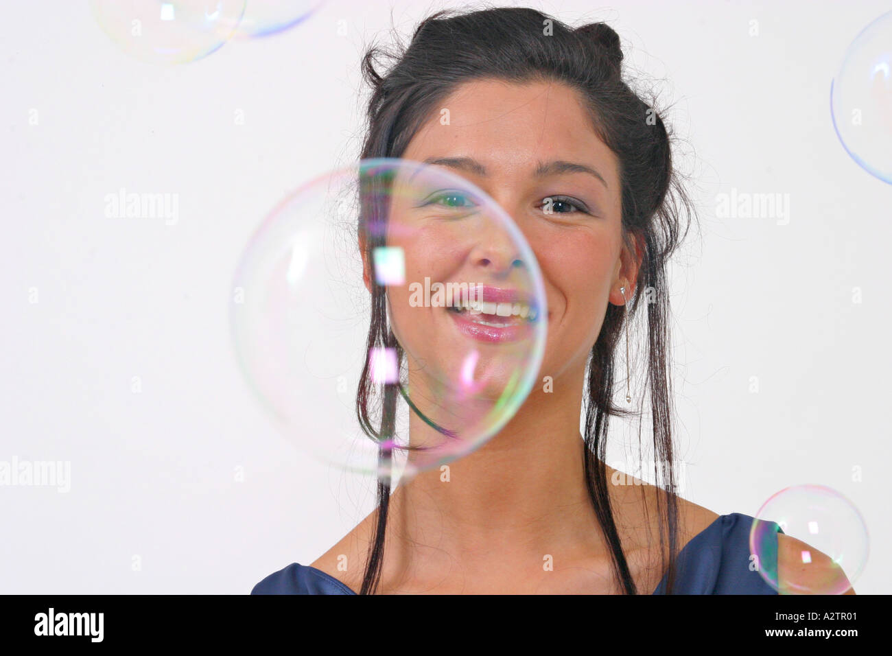 Bezugseinheiten der junge Frau in einem blauen Abendkleid mit Blick auf die Kamera durch Seifenblasen und lächelnd mit halb geöffneten Mund Stockfoto