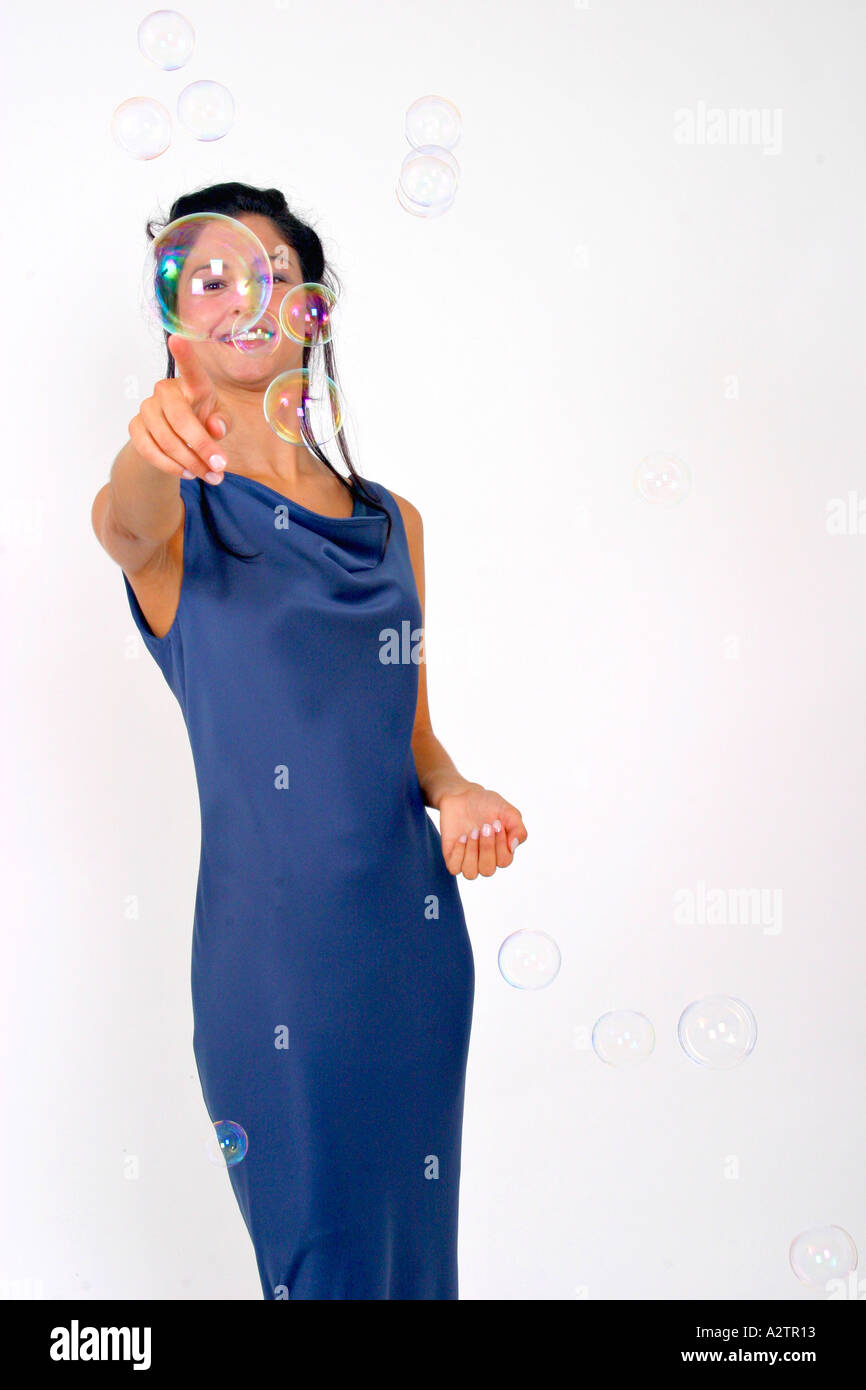 M.S. junge Frau in einem blauen Abendkleid lächelte breit, superstolz durch eine Blase und das Spiel mit Seifenblasen mit Hand und fin Stockfoto