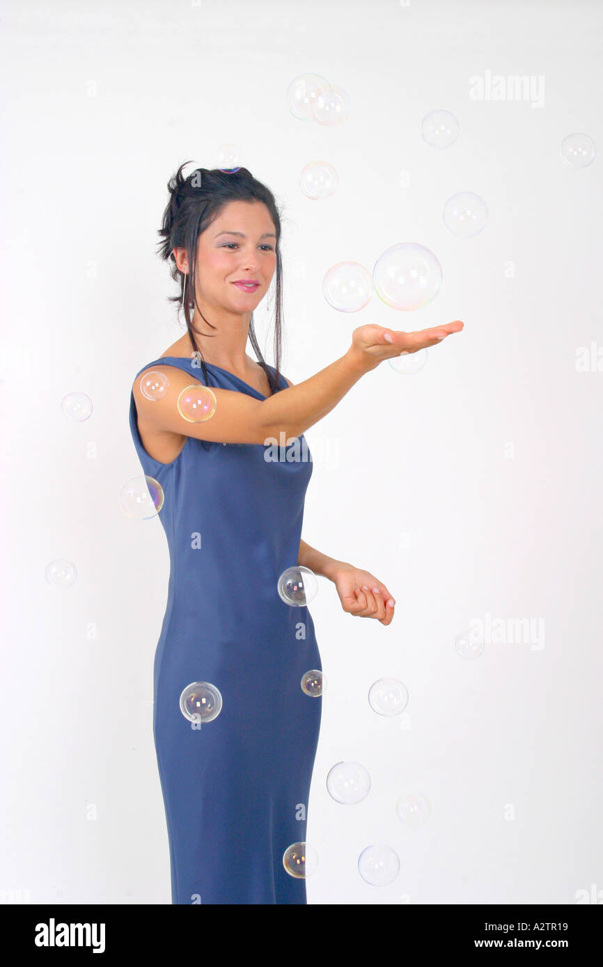 M.S. junge Frau in einem blauen Abendkleid lächelte breit, superstolz durch eine Blase und das Spiel mit Seifenblasen mit Hand erweiterten Stockfoto