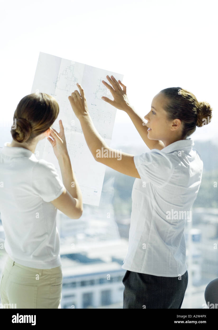 Zwei berufstätige Frauen betrachten Blaupausen und sprechen Stockfoto