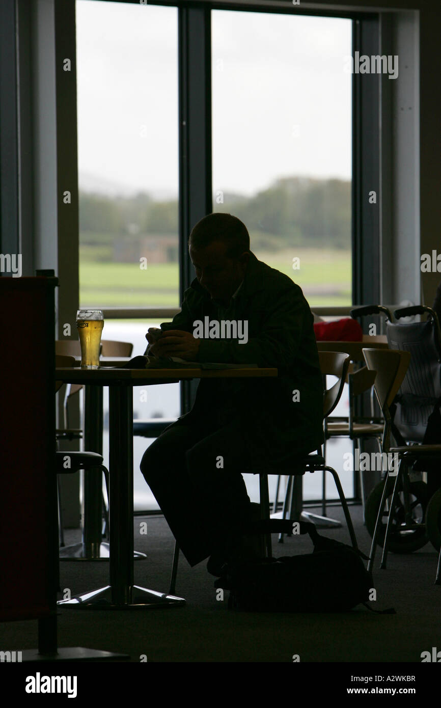 Mann in der Silhouette sitzt an einem Tisch in der Abflughalle des Belfast International Airport Stockfoto