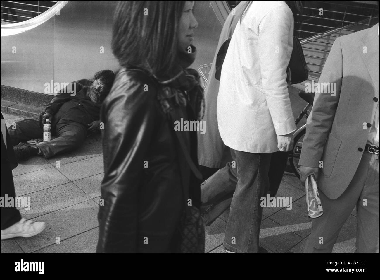 Fussgänger laufen vorbei ein Obdachloser schläft auf dem Bürgersteig vor einer Bank, Shinjuku, Tokio, Japan, Asien Stockfoto