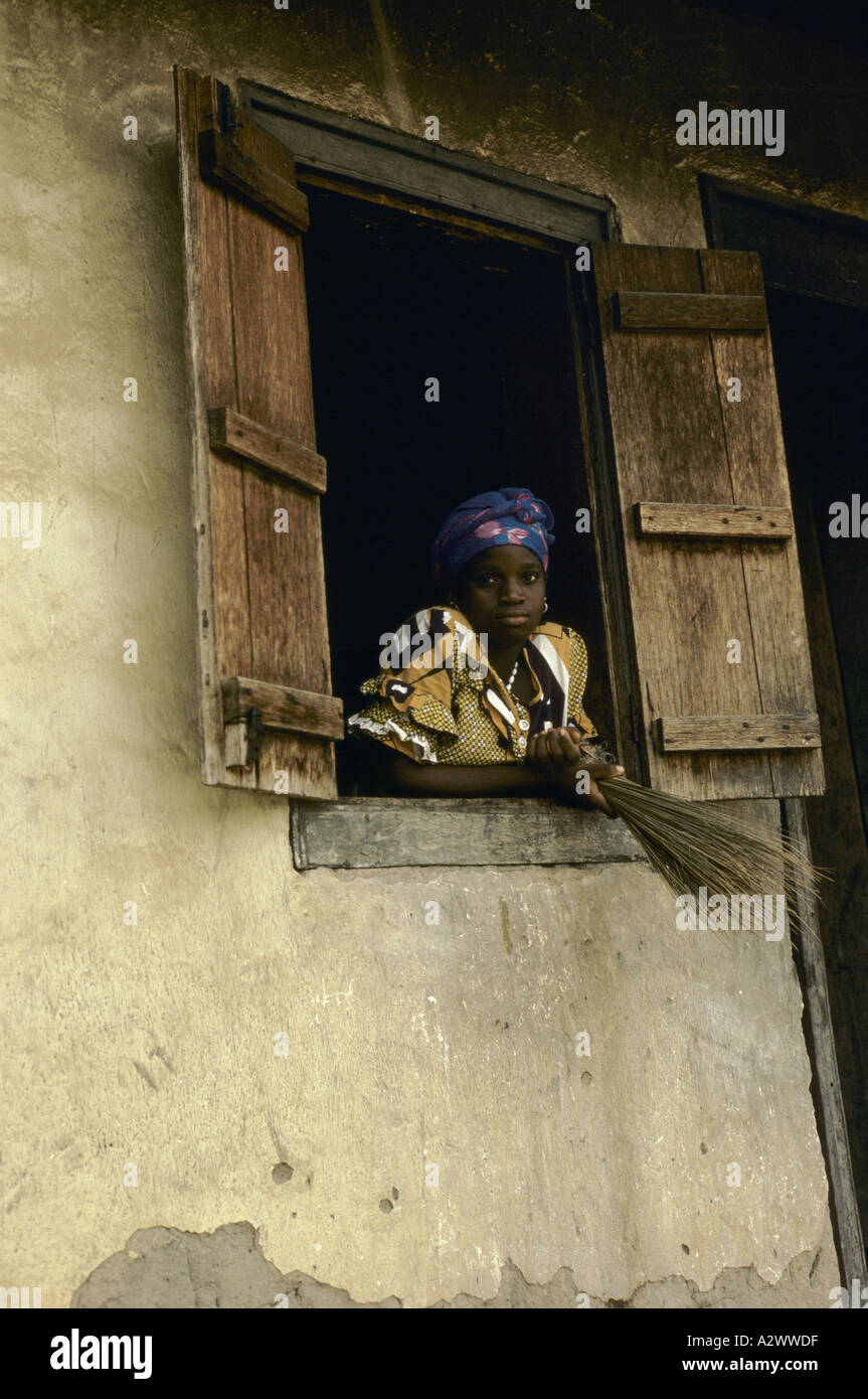 Eine Frau mit einem Pinsel lehnt aus dem Fenster. Njaluahan Dorf, Sierra Leone, Afrika Stockfoto
