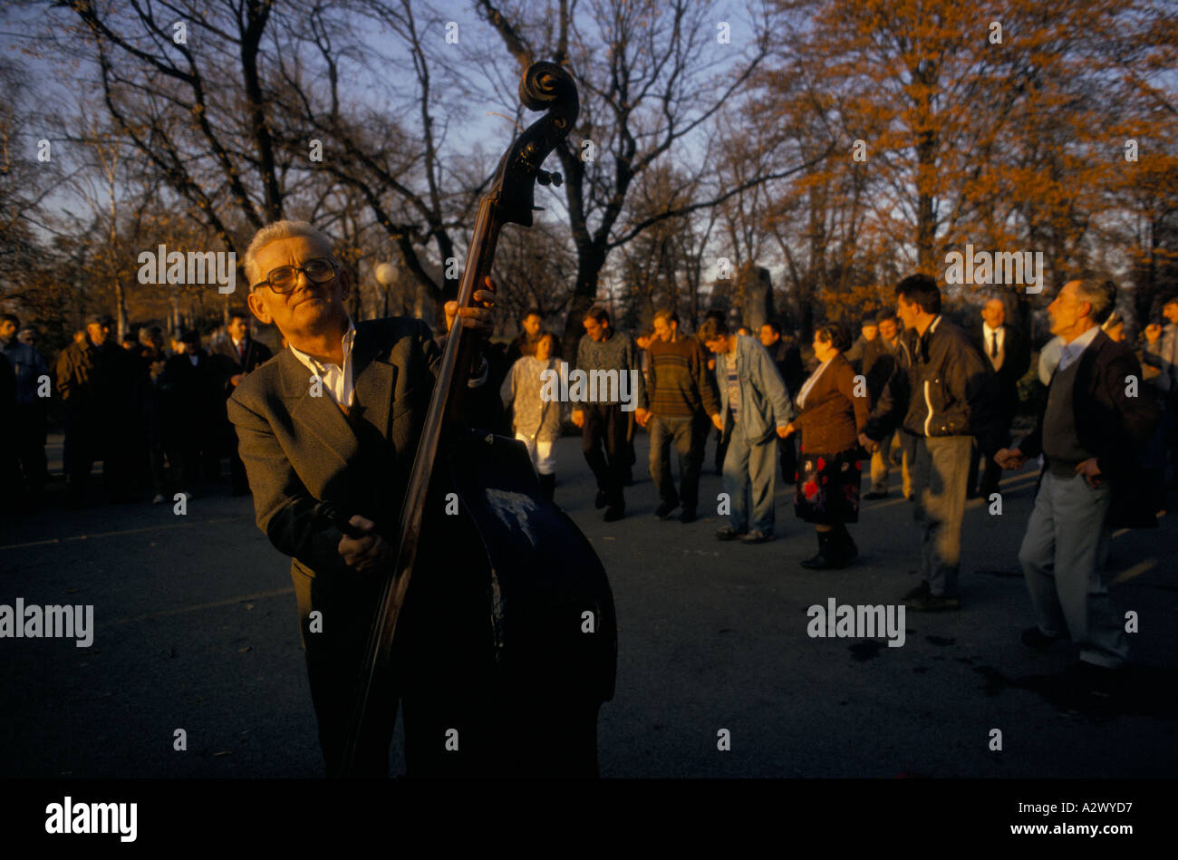 Belgrad unter Sanktionen: ein Alter Mann spielt Kontrabass, wie Leute tanzen, halten die Hände in Veliki Kalemedan Park, Dez. 1993 Stockfoto