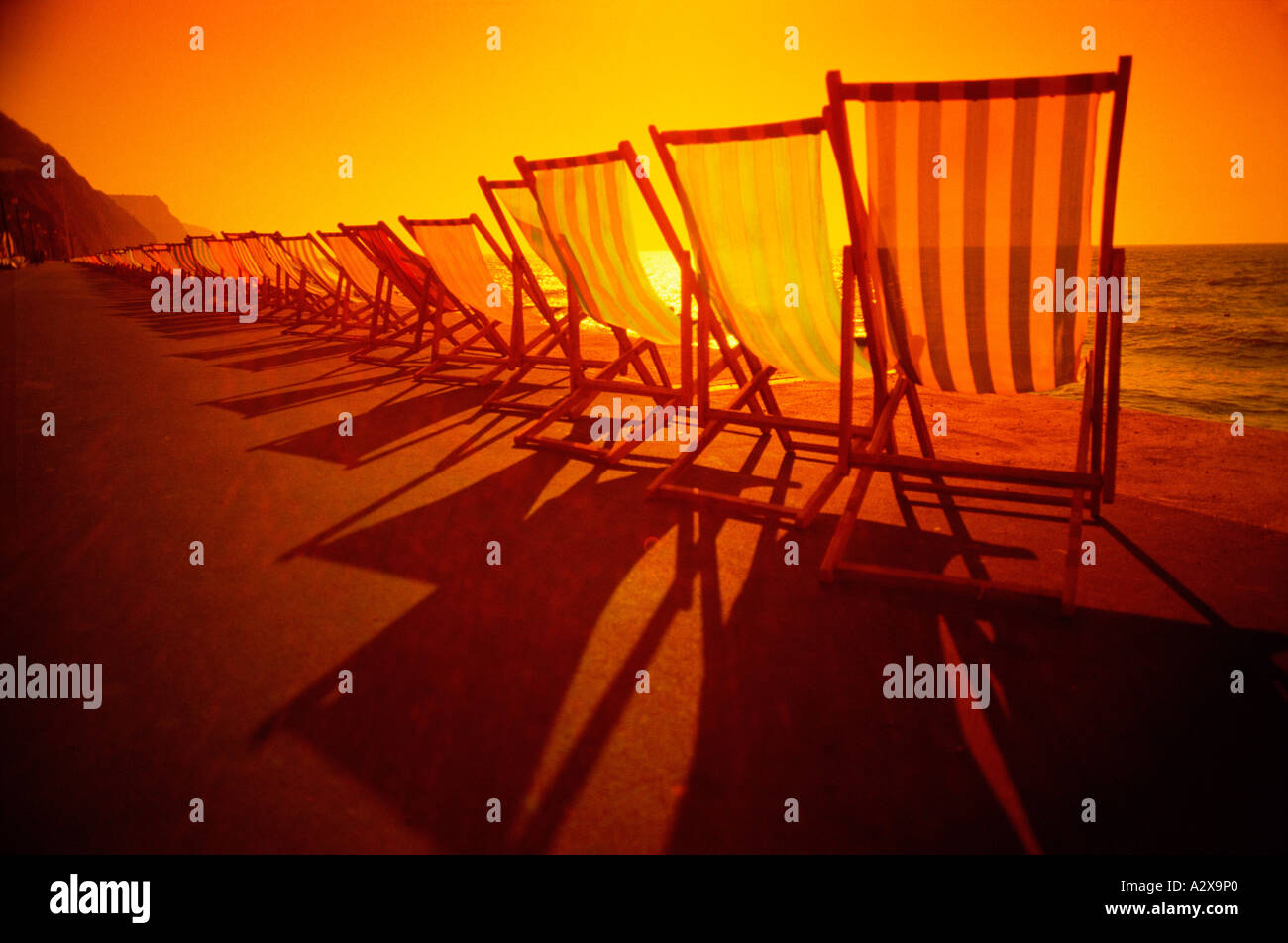 Vereinigtes Königreich. England. Reihe von Liegestühlen direkt an Strandpromenade beleuchtet wieder bei Sonnenuntergang. Stockfoto