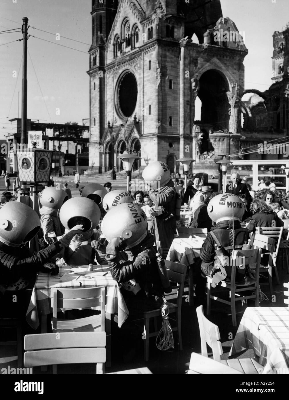 Während einige der Straßen Berlins mit ihren Bombenkratern in den 1950er Jahren noch Mondlandschaften ähnelten, publizierten diese Männer vom Mond lediglich einen Film in den westlichen Teilen der Stadt hier hat der Fotograf die Außerirdischen in einem Straßencafe überrascht Waehrend einige Strassenzuege Berlins noch Kraterlandschaften gleichen laufen diese Mondmaenner in den fuenfziger Jahren für den Film Enstation Mond im Westteil der Stadt Reklame der Fotograf der Fotograf 648 kuriöse Momente Stockfoto