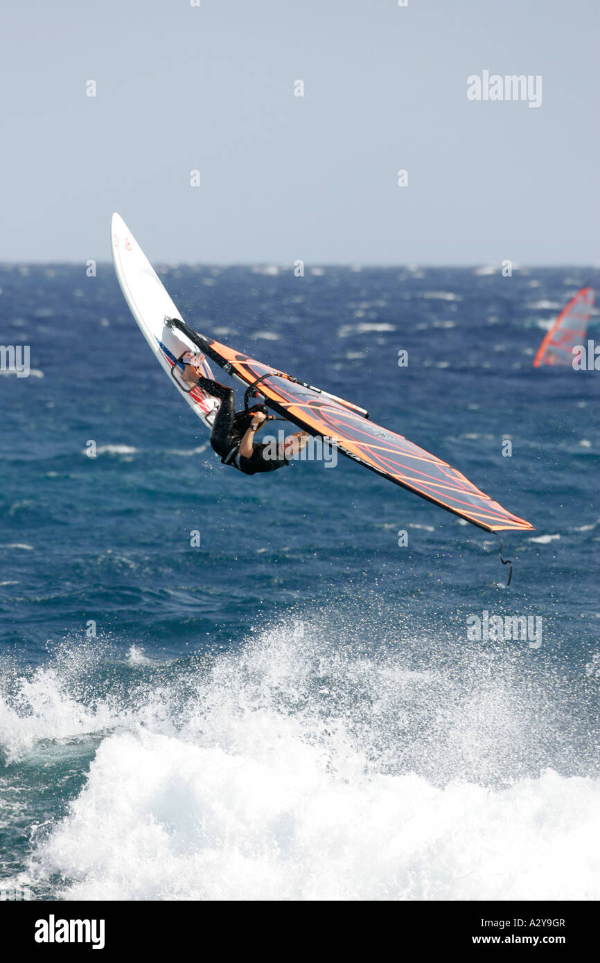 Windsurfer im Neoprenanzug startet ihr Board mit Geschwindigkeit in die Luft aus der Spitze einer Welle im Meer Stockfoto