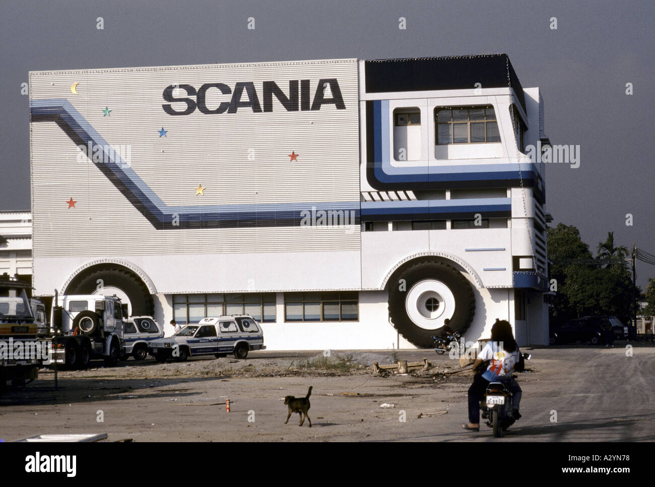 Scania Fabrikgebäude geformt wie ein grosser Lastwagen an der Airport Road, Bangkok, Thailand. Ein Mann auf einem Motorrad und einem Hund zu suchen, auf Stockfoto