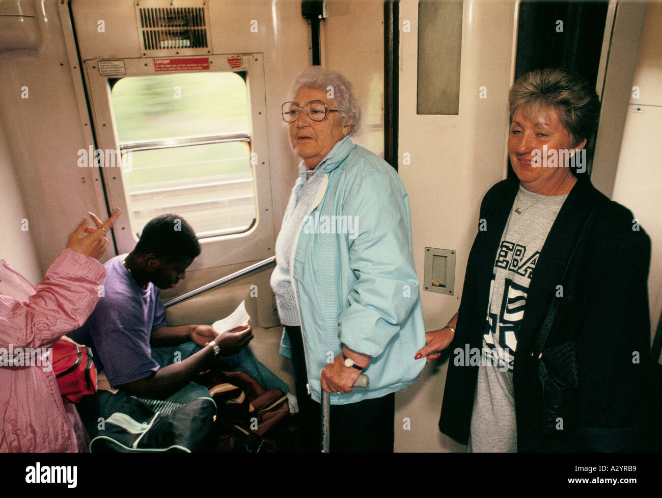 alte Frau steht auf einem überfüllten Zug mit einem Gehstock Stockfoto