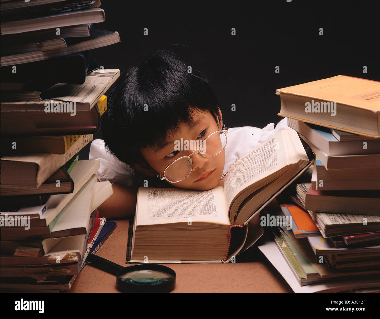 eine chinesische sieben Jahre alt legte junge seinen Kopf in den Stapel der Lehrbücher Stockfoto