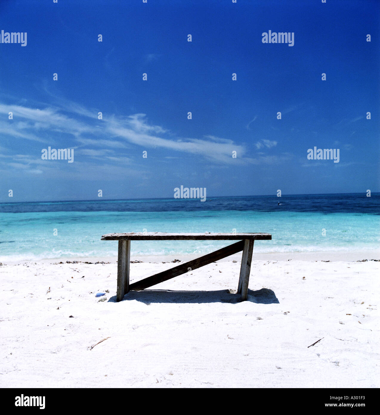 Holzbank am weißen Sandstrand und endlosen blauen Himmel und Wasser Stockfoto