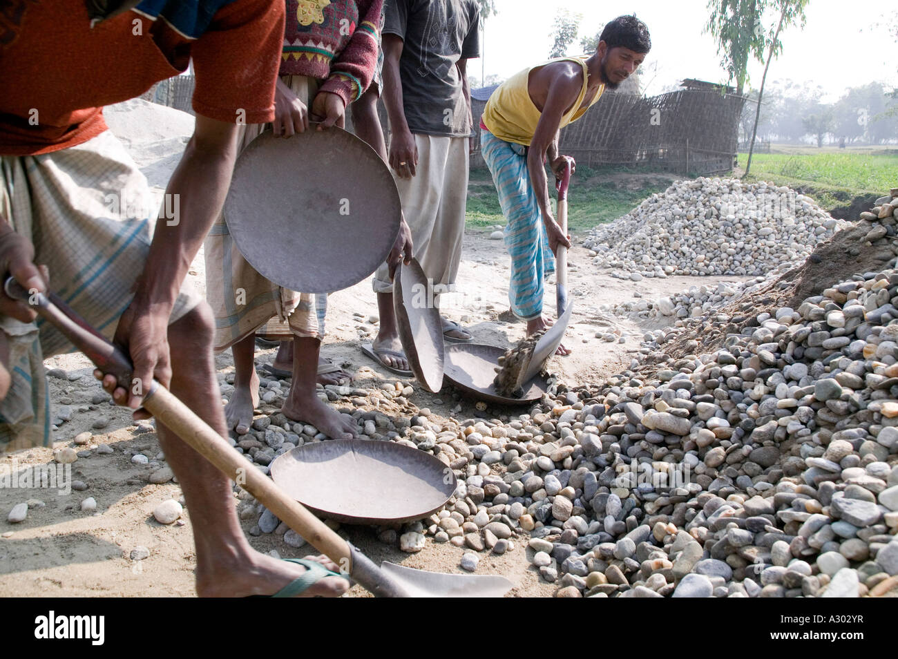 Männer Schaufeln große Felsen auf Tabletts zu einer Maschine durchgeführt werden, die sie bis auf kleinere Felsen im nördlichen Bangladesh brechen Stockfoto