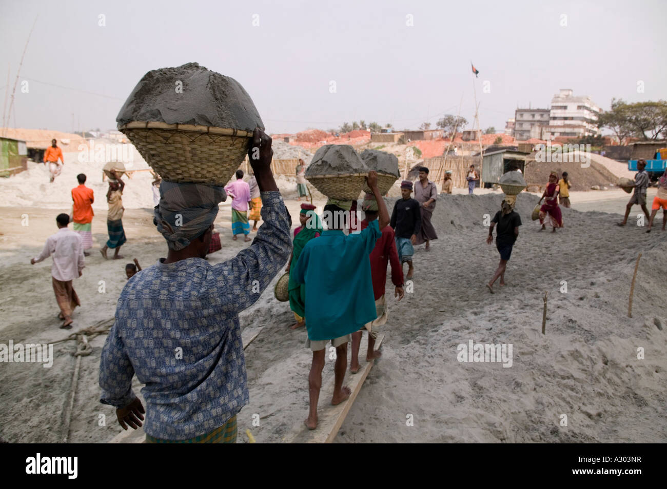 Arbeiter tragen schwere Körbe Sand auf ihre Köpfe aus dem Boot an den Strand entlang der Straße zum Savar in Bangladesch Stockfoto