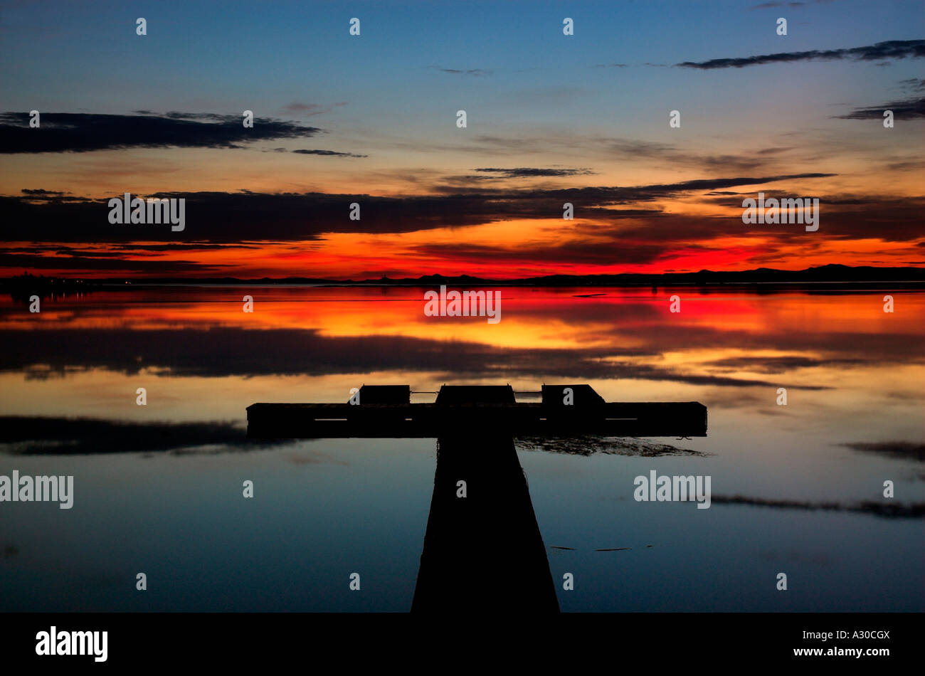 Ein roter Sonnenuntergang spiegelt sich auf eine perfekt noch Lagune mit einem Steg Stockfoto