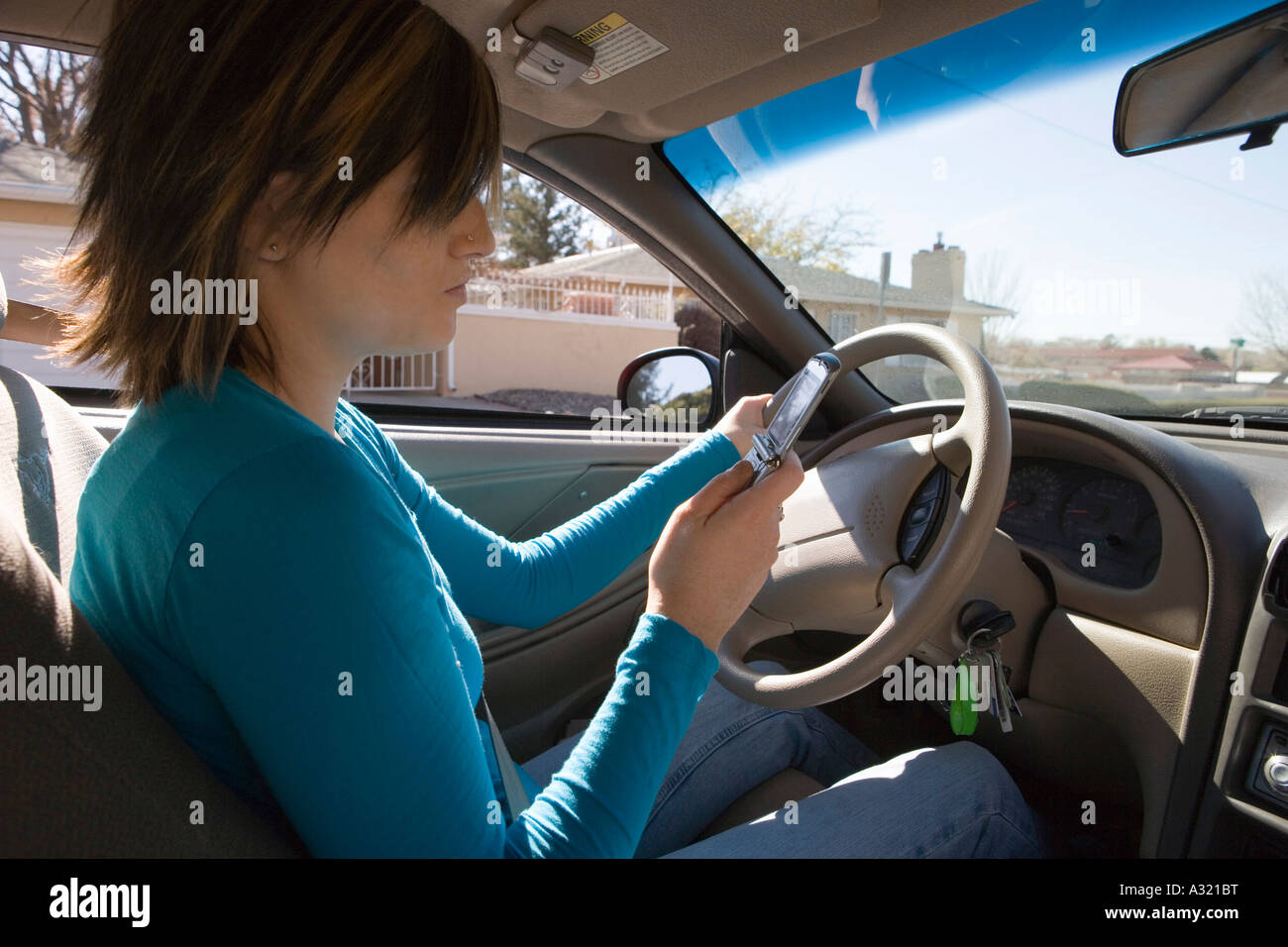 Junge Frau im Fahrersitz eines Autos sitzen und mit Blick auf Handy Stockfoto