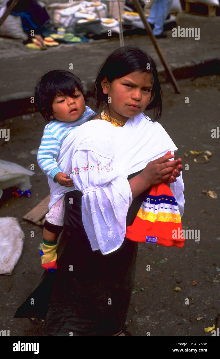 Ein junges Otavalan Mädchen mit einem kleinen Kind auf dem Rücken in Otavalo Ecuador Stockfoto