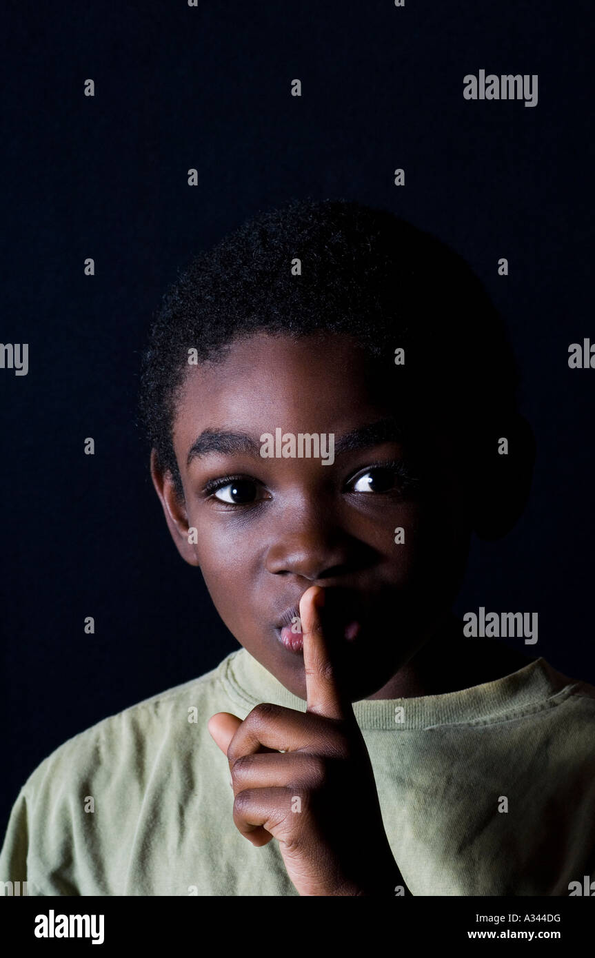 Schelmische Junge mit seinem Finger auf seinen Mund auf schwarzem Hintergrund Stockfoto
