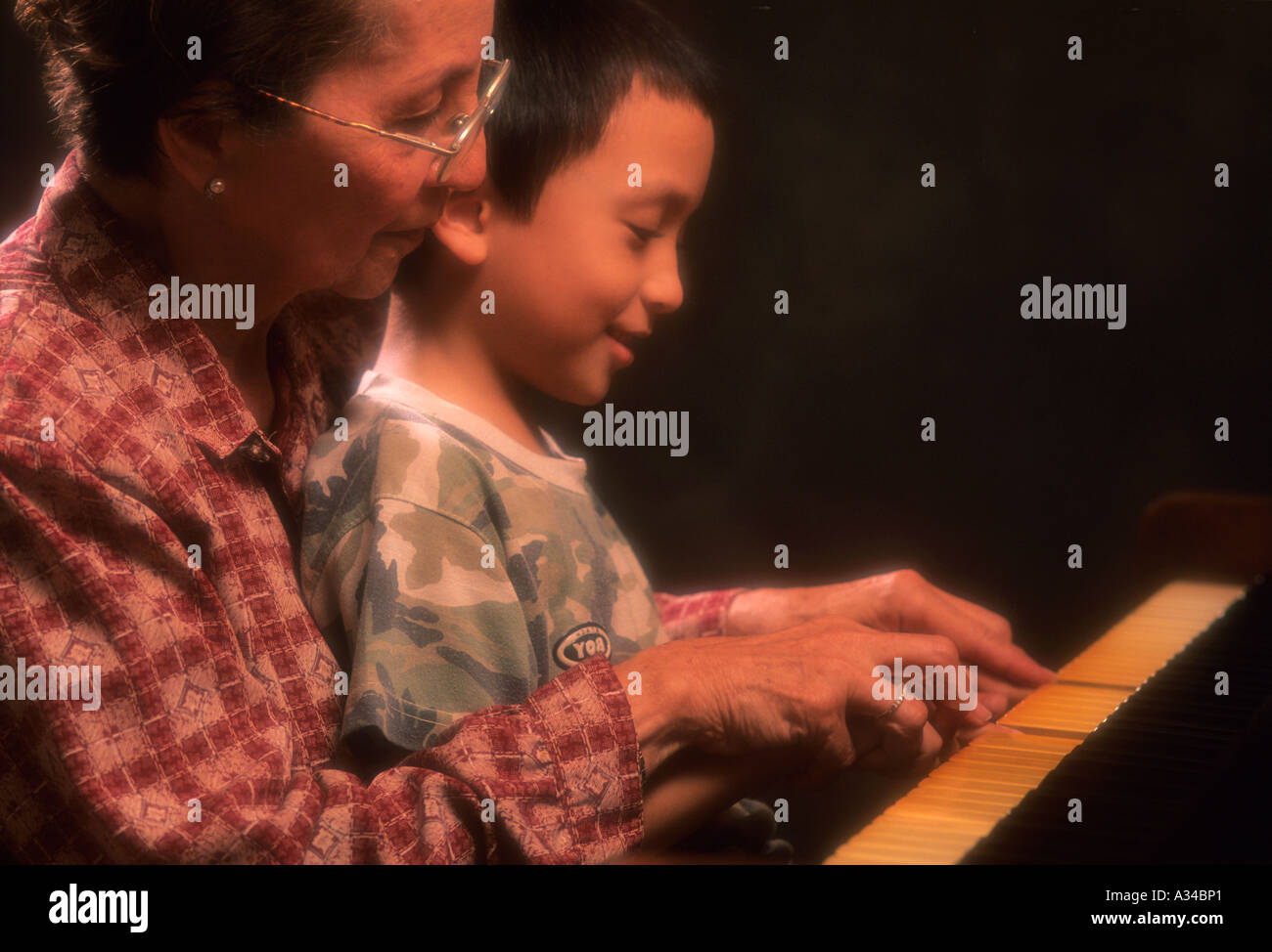 Eine Großmutter lehrt ihren Enkel, wie man Klavier spielen. Stockfoto