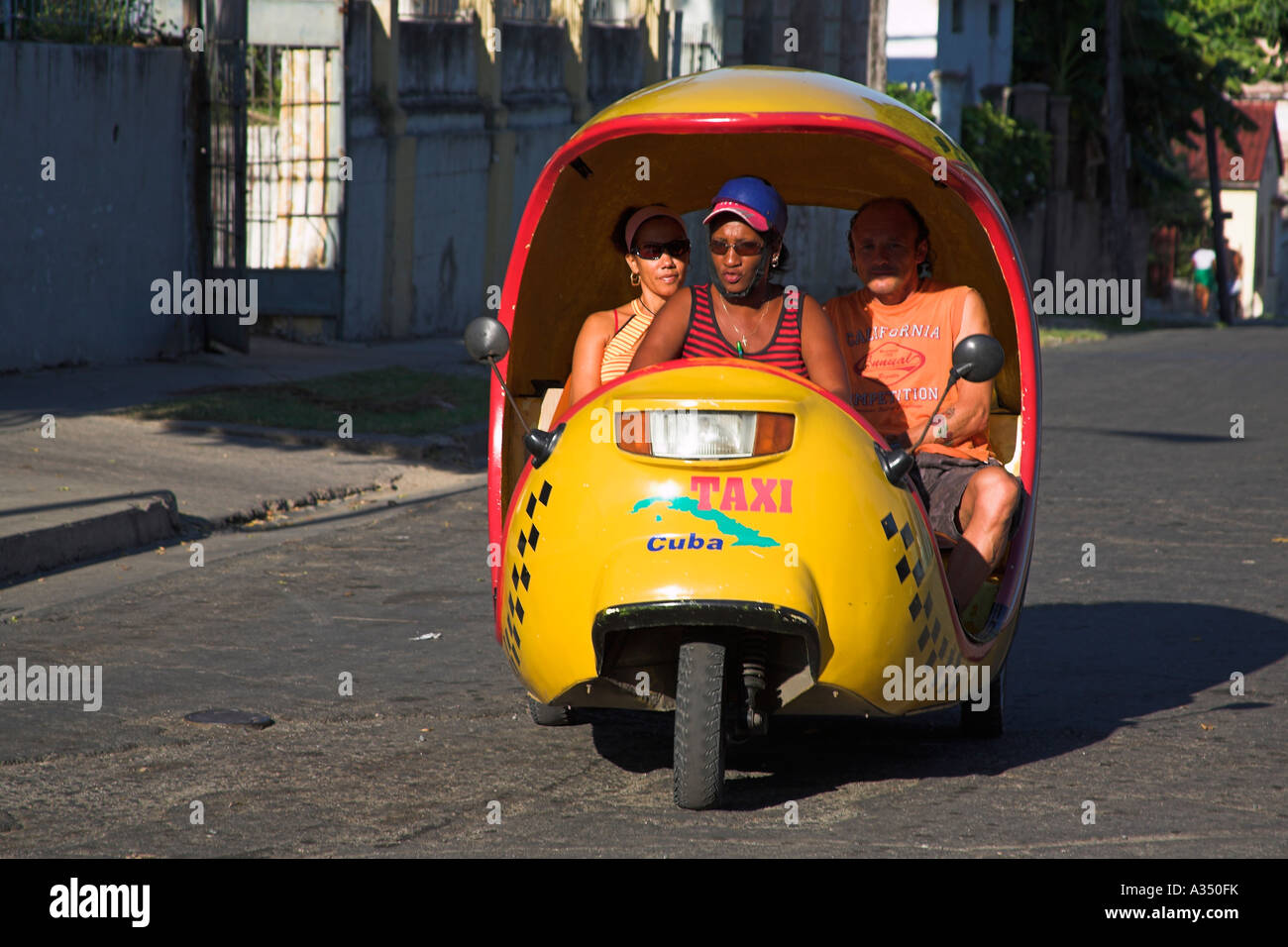 Fahrer und Passagiere in gelb drei Rädern Taxi, Santiago De Cuba, Kuba Stockfoto