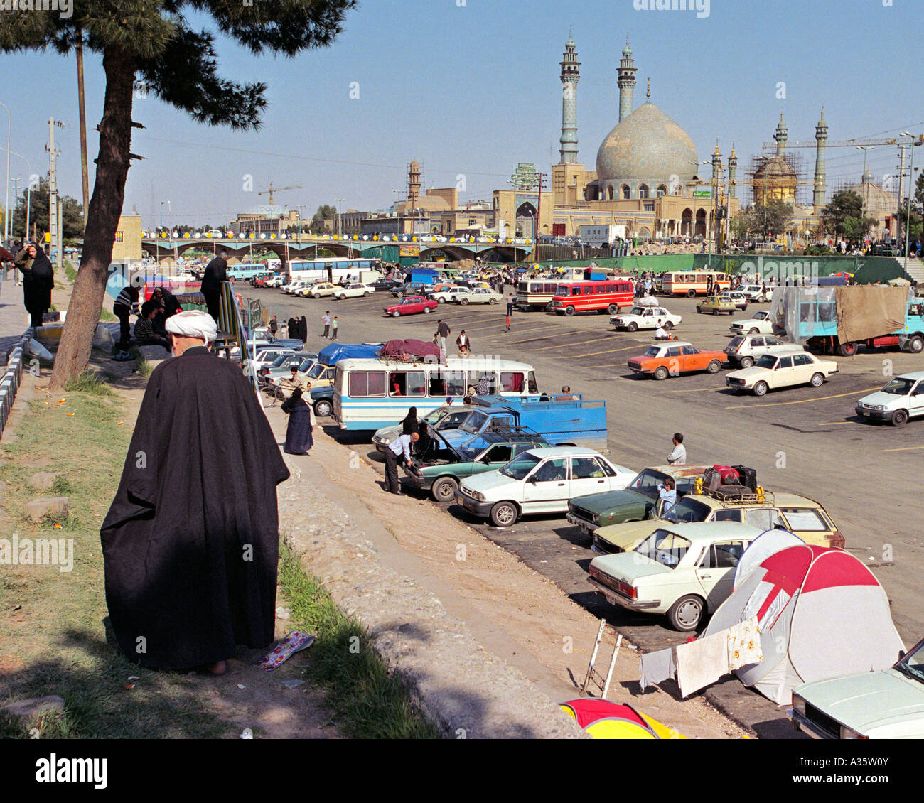 Ein Mullah Spaziergänge entlang des Ufers über das trockene Bett des Flusses Qom mit dem Hazrat-e Masumeh Schrein im Hintergrund. Qom, Iran Stockfoto