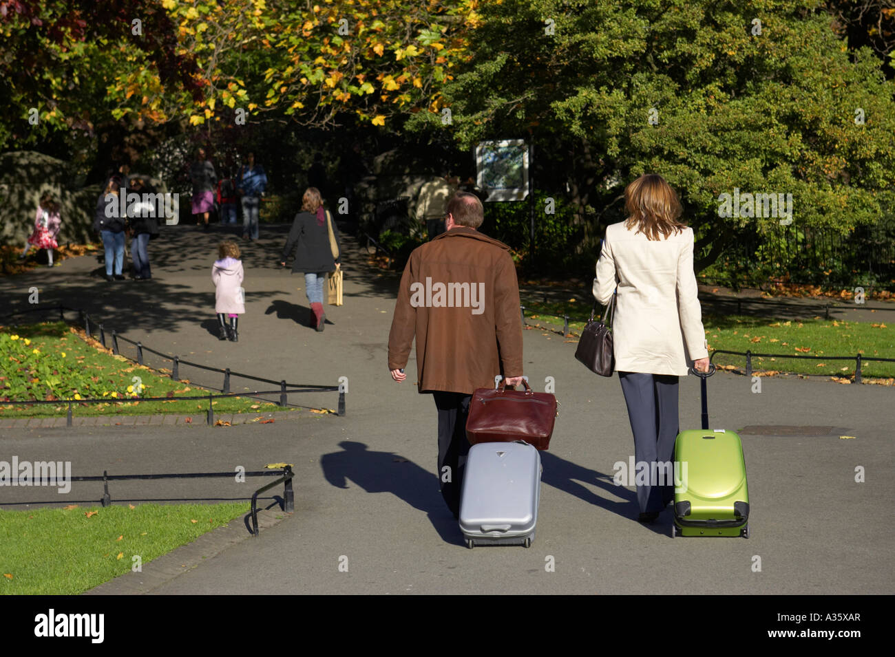 männliche und weibliche Geschäftsreisende ziehen Rädern Gepäck durch den Park St. Stephens Green Dublin City Centre Stockfoto
