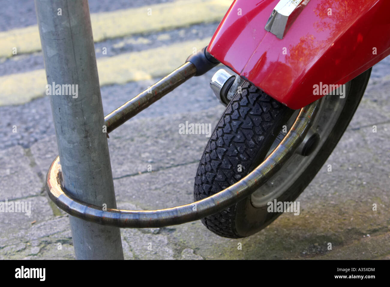 roter Motorroller an Metallpfosten mit Sicherheitskette neben gelben Doppellinien in Dublin gesichert Stockfoto