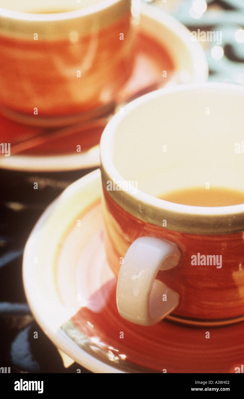 Nahaufnahme von zwei orange Tassen mit Untertassen mit Tee oder Kaffee Bodensatz auf einem dunklen Grün Schmiedeeisen Tisch Stockfoto