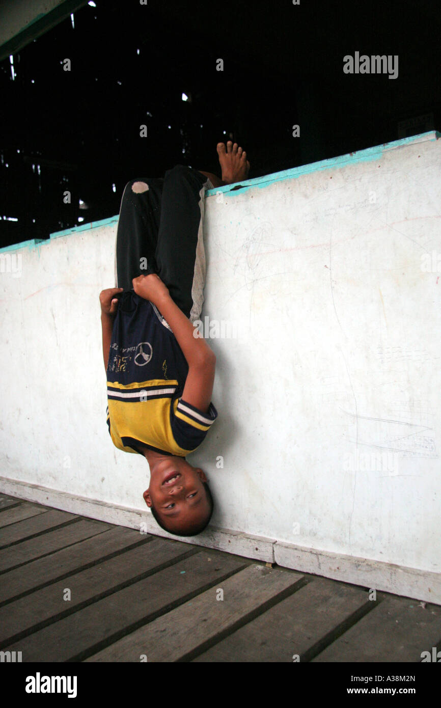 Junge, kopfüber hängend, spielen mit Freunden in seinem Langhaus an den Ufern des Sungai Terika, Sarawak, Borneo, Malaysia Stockfoto