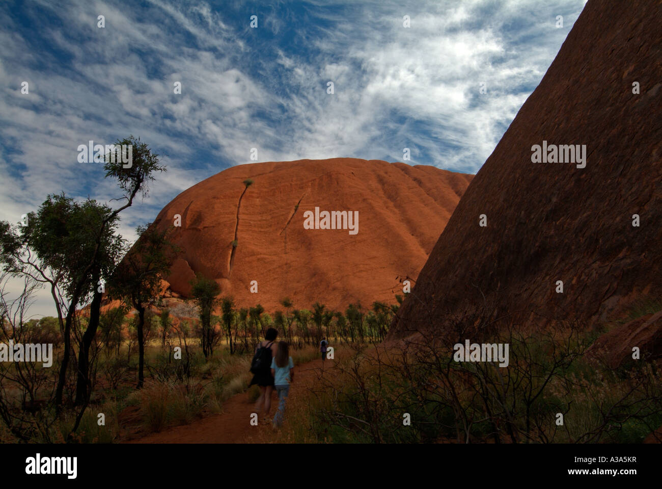 Zwei Touristen zu Fuß Wandern Ayers rock kurz nach Sonnenaufgang entlang der Basis gehen um Uluru mit Peeling im Vordergrund Stockfoto