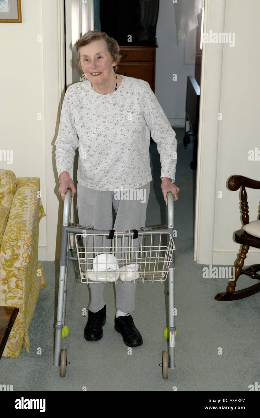Lächelnde ältere Frau geht durch ihr Wohnzimmer mit Hilfe von einem walker Stockfoto