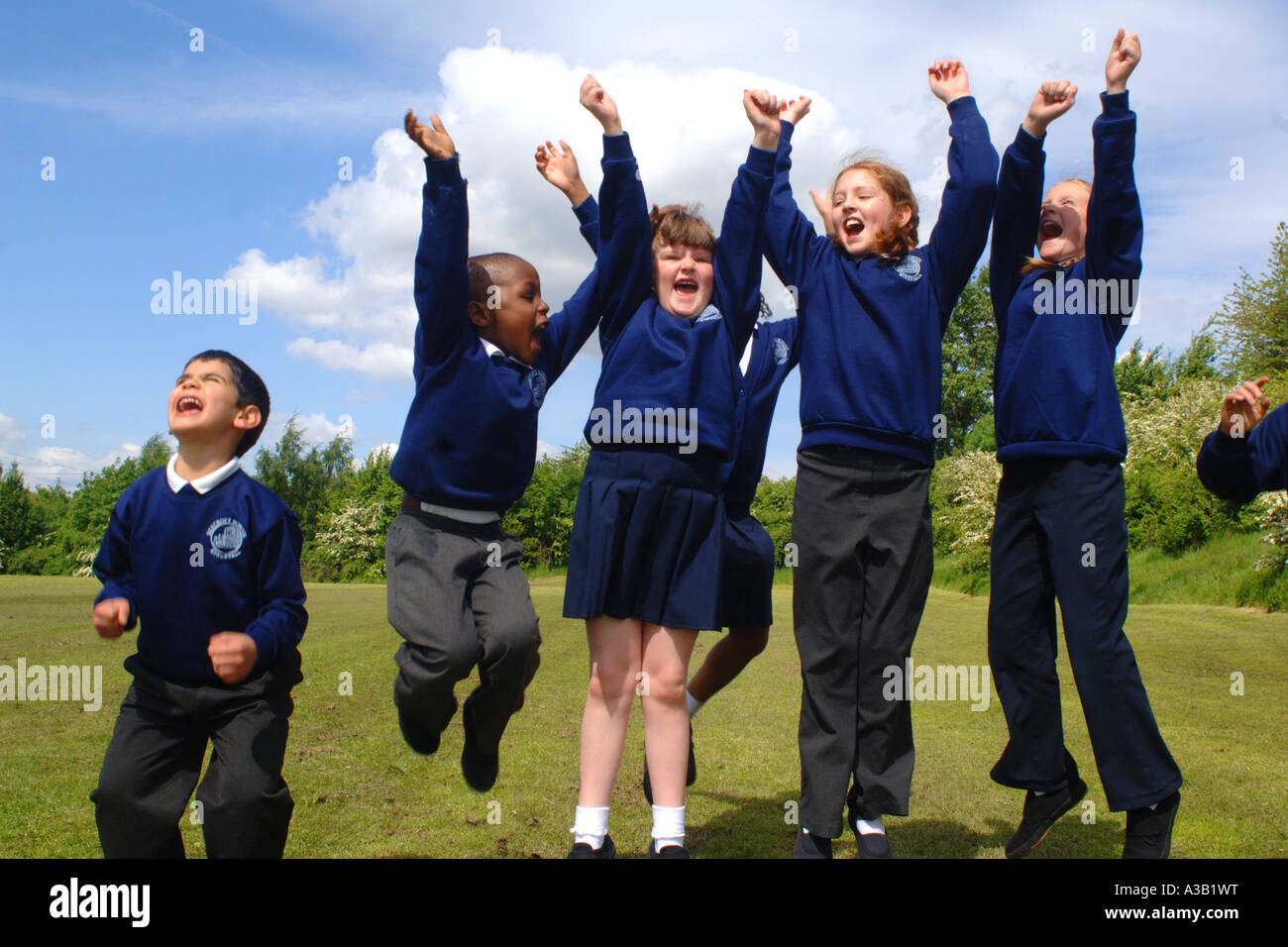 Gemischte Gruppe von Grundschulkindern jubeln ihren Freunden auf dem Spielfeld Schule Stockfoto